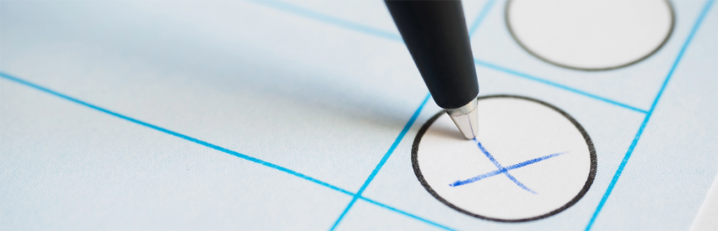 Ein Stift kreuzt ein Feld auf einem Wahlpapier an. 